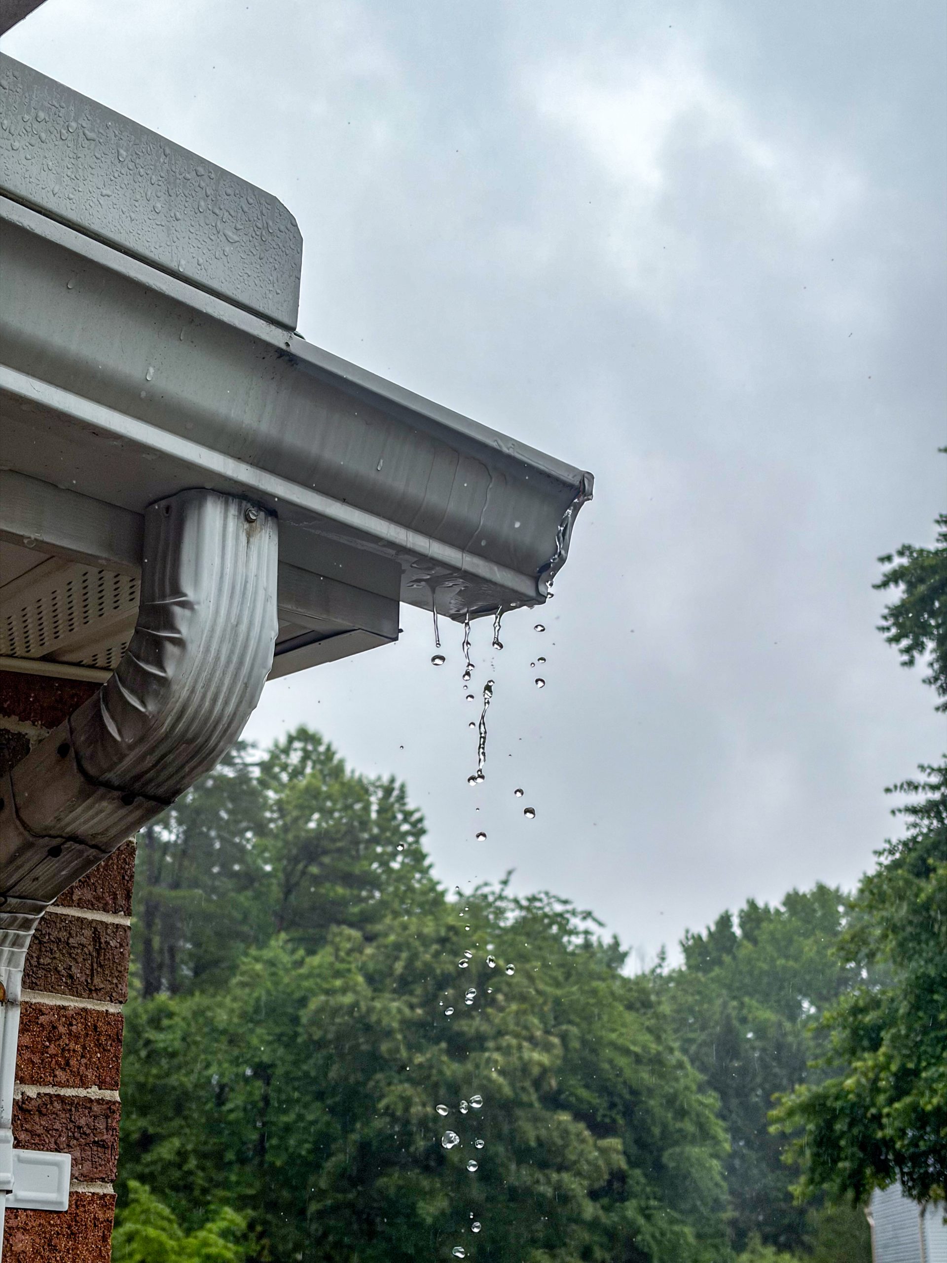 Rain dripping from a residential gutter and downspout during a storm