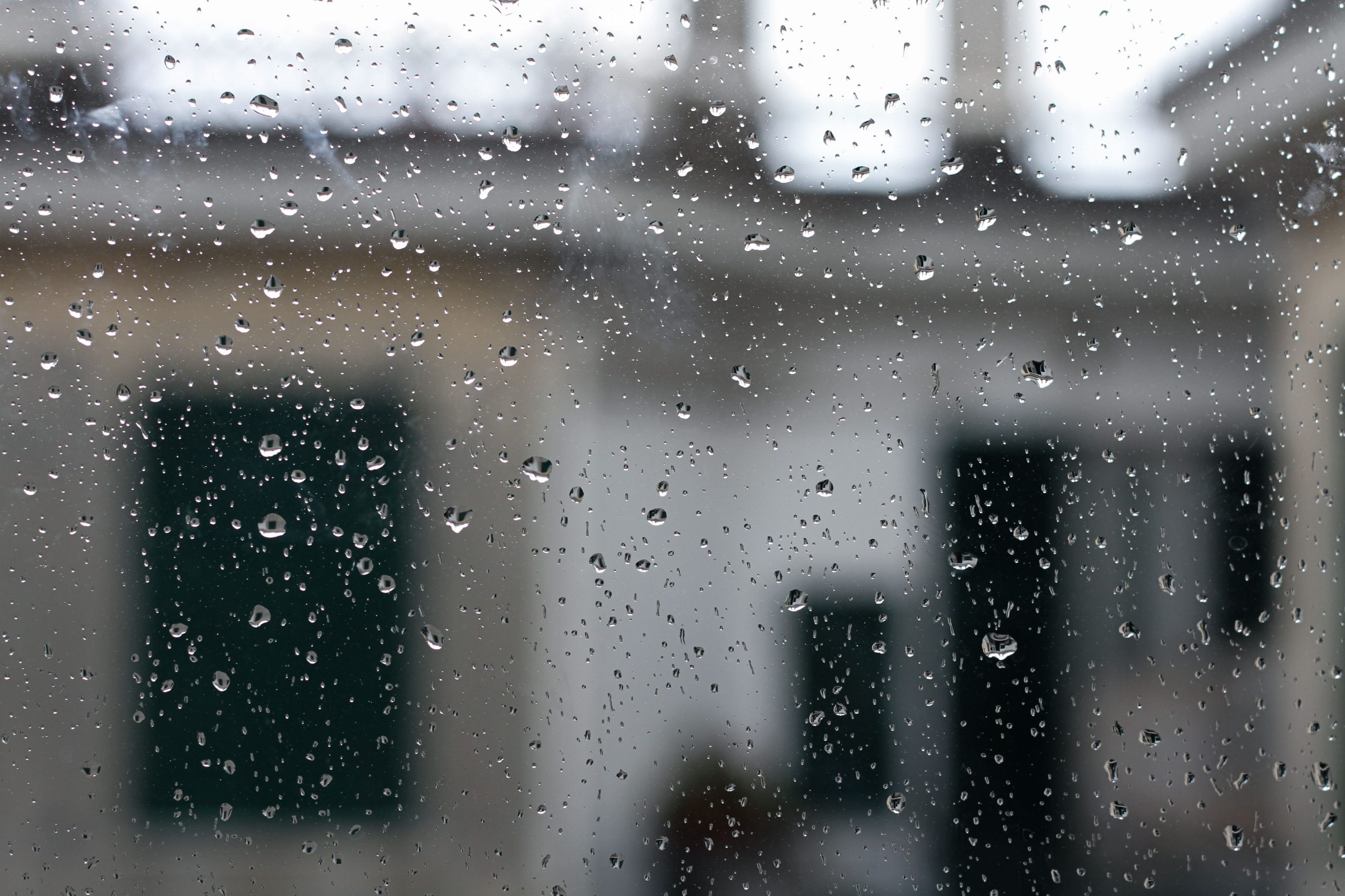 Rain streaking down a window during a storm with a house blurred in the background