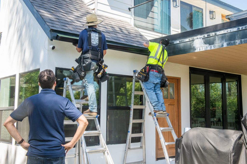 Crew on ladders installing seamless gutters on a modern home
