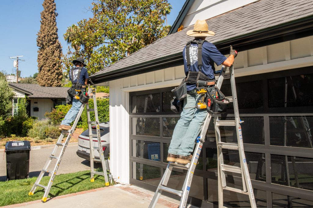 Two Solutionists installing gutters on a garage roofline