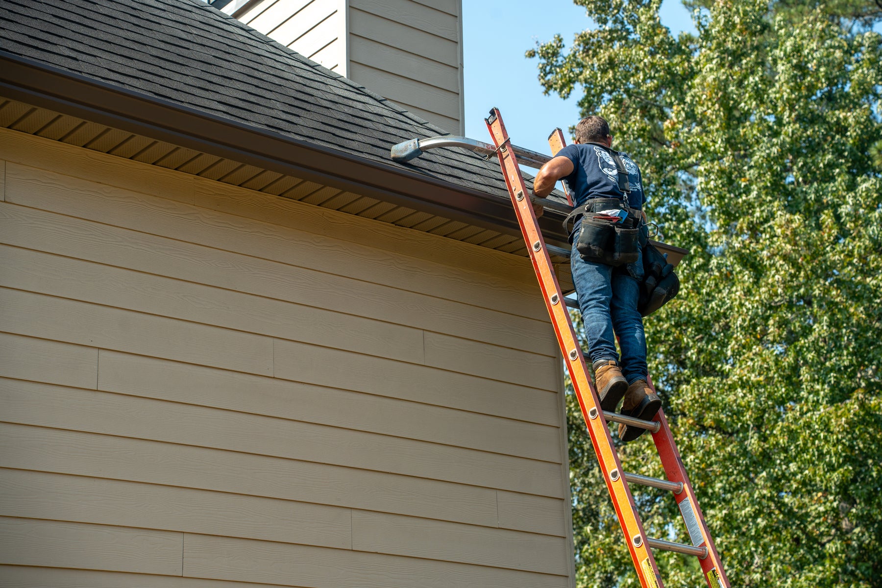A Brothers That Just Do Gutters technician on a ladder servicing a gutter run