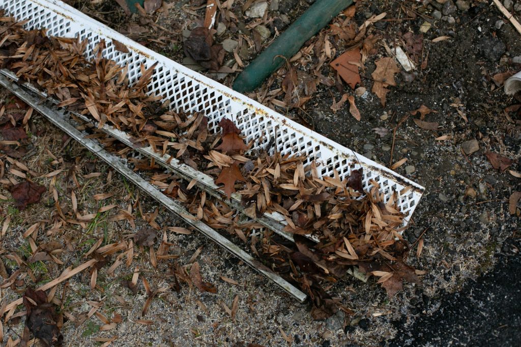 An old plastic leaf guard packed with leaves