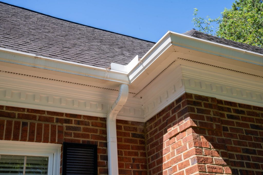 A white gutter and downspout at a brick corner